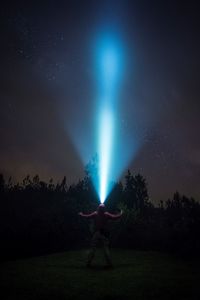 Silhouette man standing by illuminated tree against sky at night