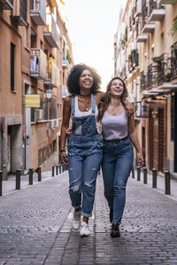 Full length portrait of smiling woman walking on footpath in city