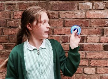 Girl playing with fidget spinner against brick wall