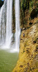 Mid distance of woman standing on rock formation against waterfall