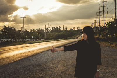 Woman standing on road against sky during sunset