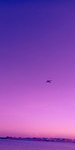 Airplane flying over sea against sky during sunset