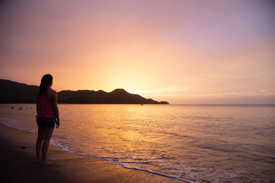 Rear view of man standing on beach during sunset