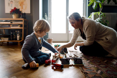 Mother and daughter playing with toy train while sitting on hardwood floor in living room