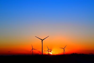 Silhouette wind turbines on landscape against sky during sunset