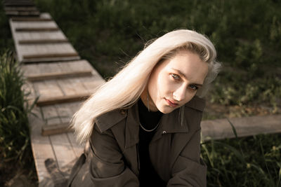 Portrait of young woman sitting on wooden plank outdoors