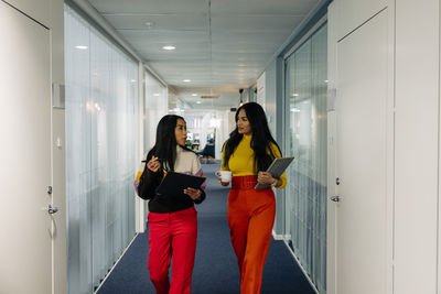 Female business colleagues discussing while walking in corridor at office