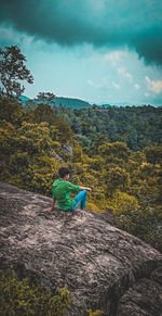 Rear view of man sitting on mountain against sky