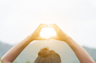 Cropped image of woman making heart shape against bright sun