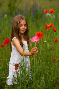 Portrait of young woman standing amidst flowers on field