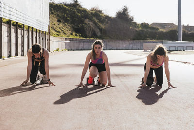 Sportswomen kneeling while preparing for race during sunny day
