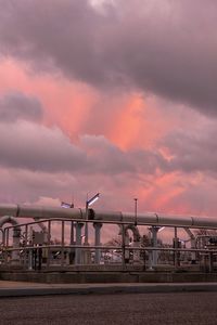 Bridge over factory against sky at sunset