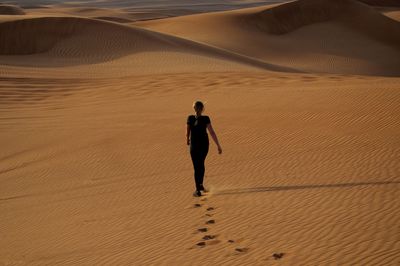 Rear view of woman walking on sand in desert