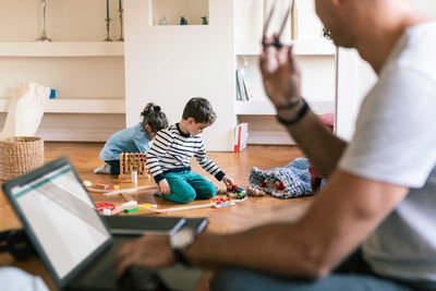 Father with laptop looking at children playing at home