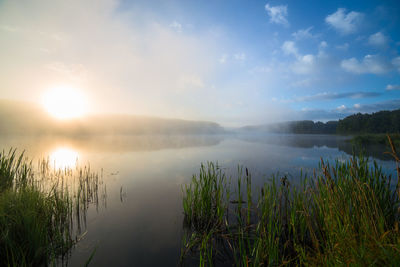 Scenic view of foggy lake or river against sky during sunrise