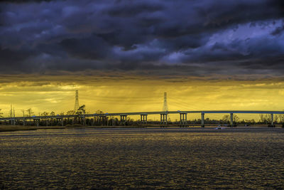 Bridge over river against dramatic sky during sunset