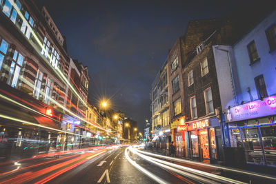 Light trails on city street amidst buildings at night