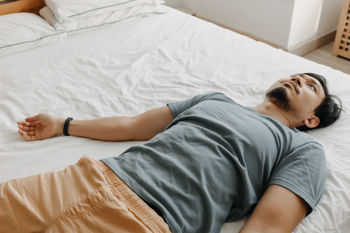 Tired man is lying on the bed as he out of energy.