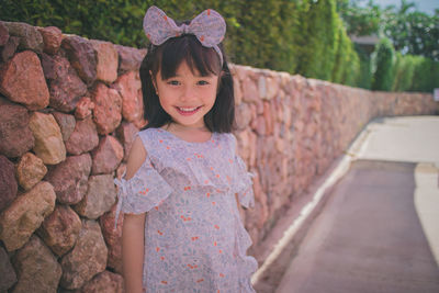 Portrait of smiling girl wearing headband standing against stone wall