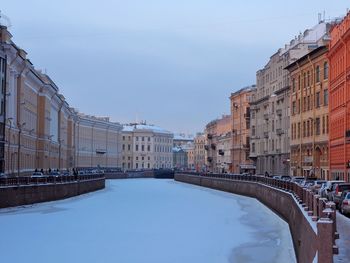 Buildings by frozen canal against sky in city