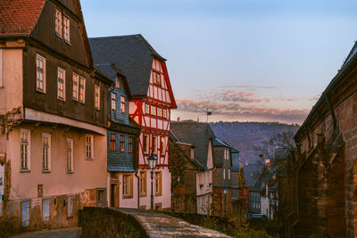 Houses by buildings in town against sky during sunset