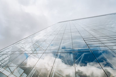 Low angle view of glass building against cloudy sky