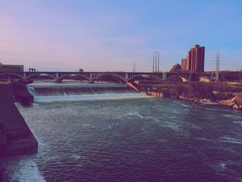 Bridge over river by buildings against sky