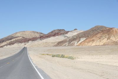 Road leading towards mountains against clear sky