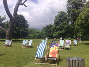 Deck chairs on grass against trees against sky