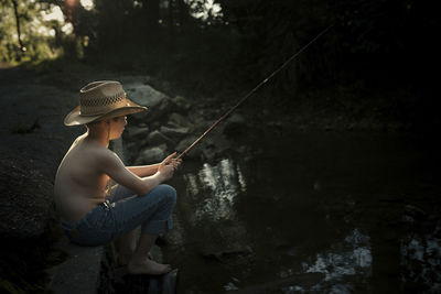 Boy fishing in lake while sitting on rock