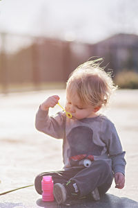 Full length of cute boy blowing bubble while sitting on street during sunny day