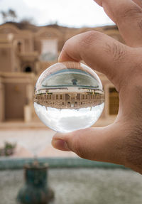 Close-up of hand holding crystal ball against built structure