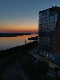 Buildings by road against sky during sunset