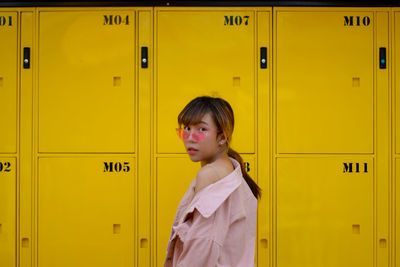 Side view portrait of young woman standing by yellow doors