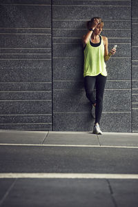 Young jogger with cell phone against grey wall