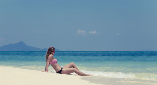 Woman sitting on beach against sky