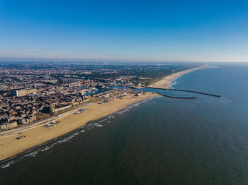 High angle view of cityscape by sea against blue sky