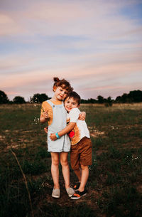 Young brother and sister standing outside hugging at sunset