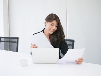 Smiling woman holding papers by laptop on desk