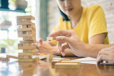 Cropped hand of man stacking wooden blocks by friend sitting on table