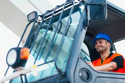 Low angle view of smiling manual worker driving vehicle