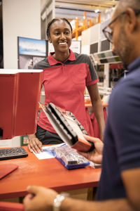 Smiling female cashier looking at male customer holding merchandise at checkout counter