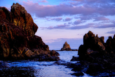 Rocks in sea against sky during sunset