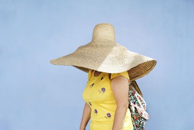 Woman wearing large hat standing against blue wall