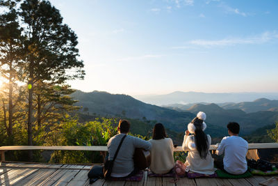 Rear view of people sitting on bench looking at mountains