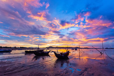 Fishing boats moored on sea against sky during sunset