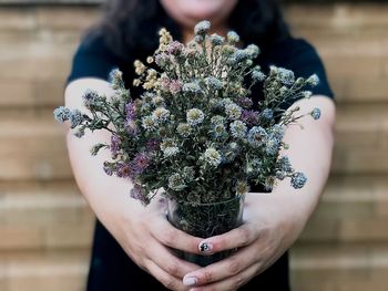 Midsection of woman holding flowers in glass