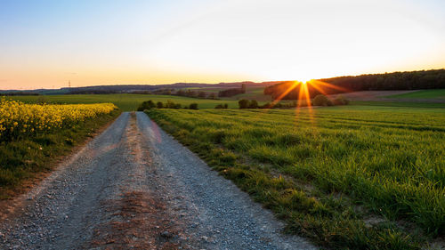 Road amidst field against sky during sunset