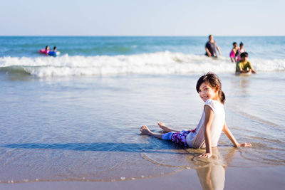 Portrait of smiling cute girl sitting on shore at beach