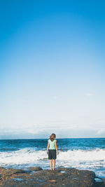 Rear view of woman standing on rock by sea against sky